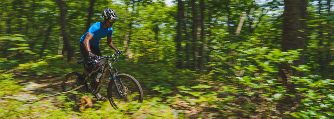 A teenage rider with googles pedals swiftly through a densely forested green landscape in Maryland
