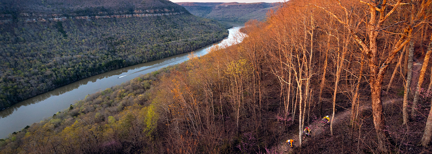 Aerial view of three mountain bikers riding among fall trees above a river gorge