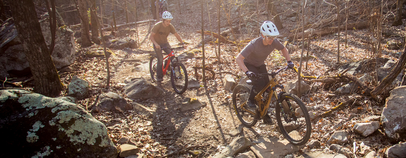 Two mountain bikers ride through a rocky, forested landscape