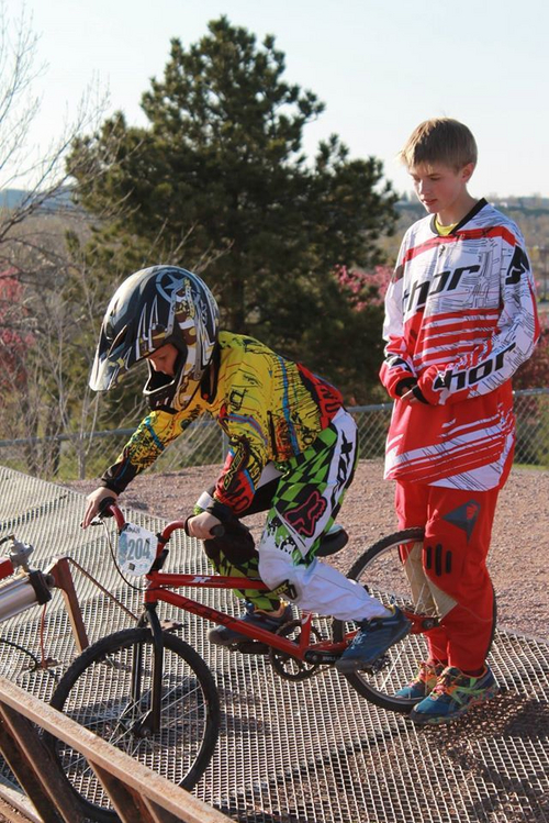 "Adam waiting for the gate to drop at BMX race, with an older kid cheering him on"