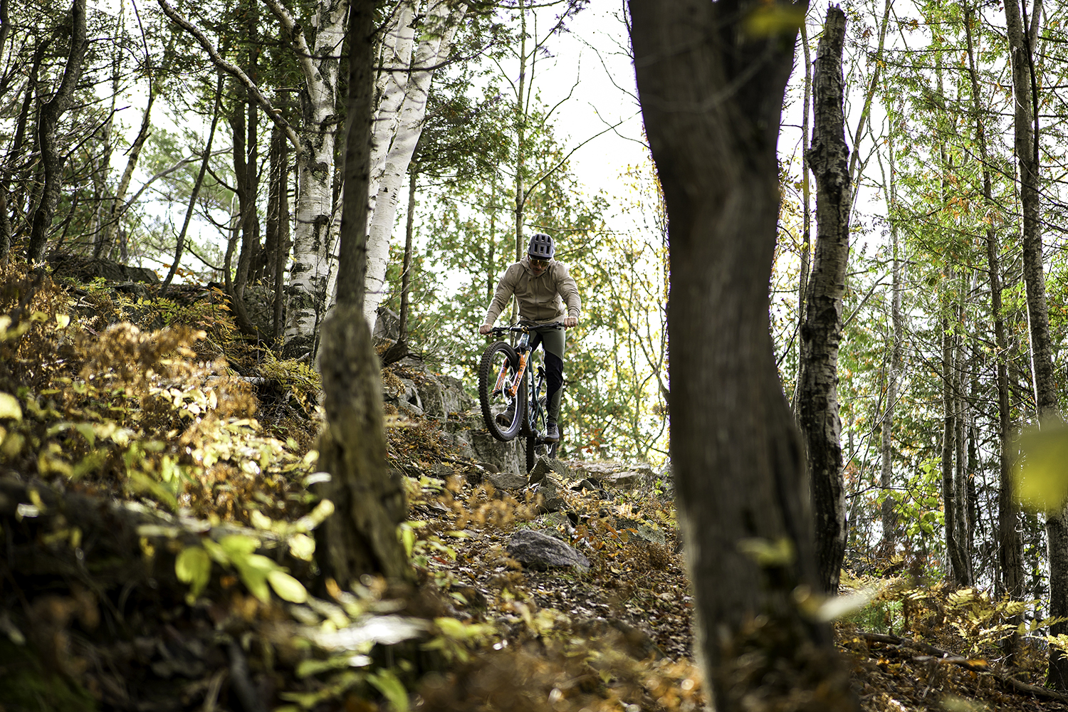 "Brice Shirbach lifting his front wheel while riding a trail filled with Autumn leaves."