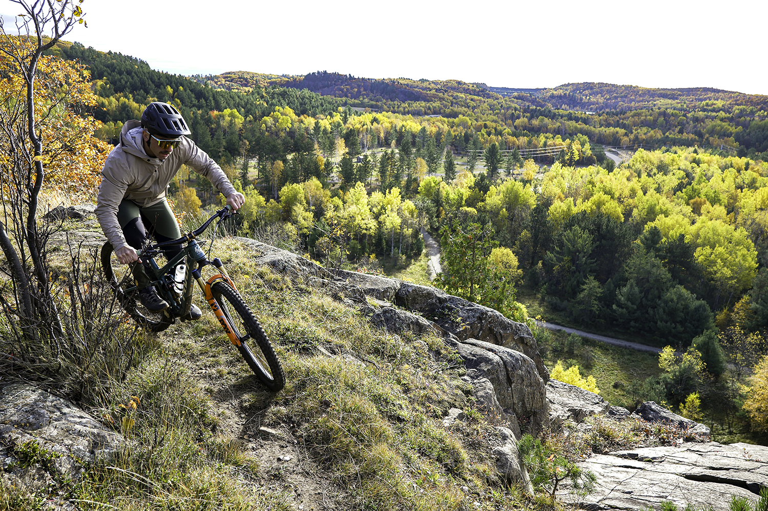 "Brice Shirbach riding a mountain bike along a cliff edge overlooking Autumn colors."