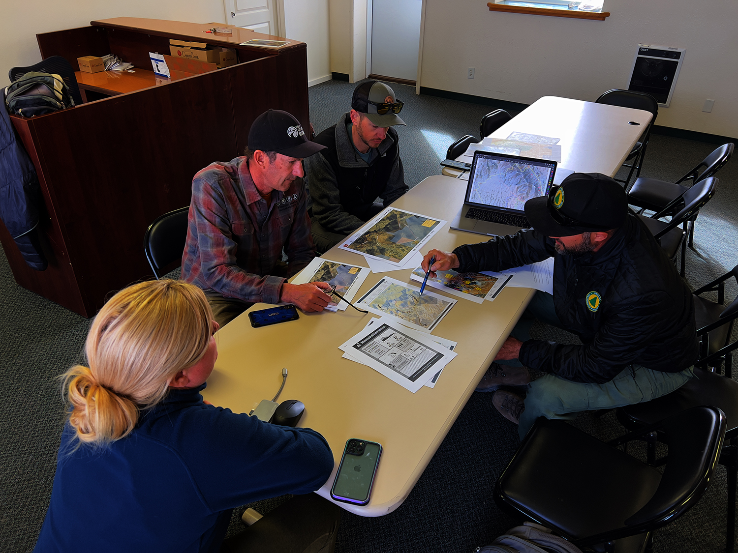 "Five people sitting at a table looking over GIS planning documents in an office setting."