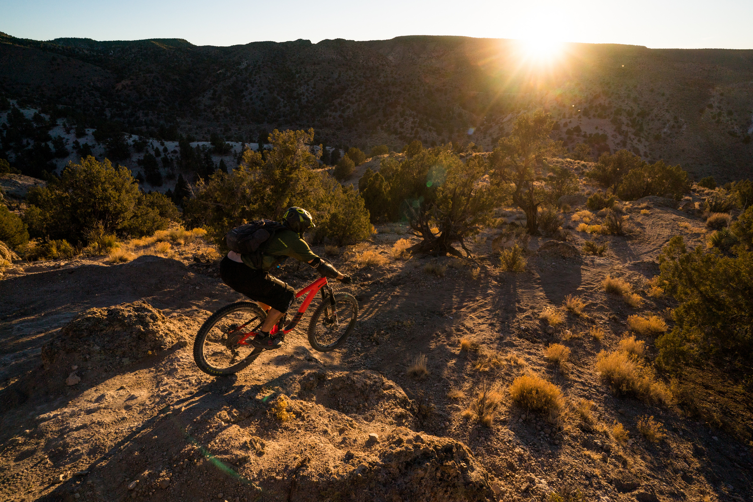 "Mountain biker dropping off a large rock feature in a desert environment."