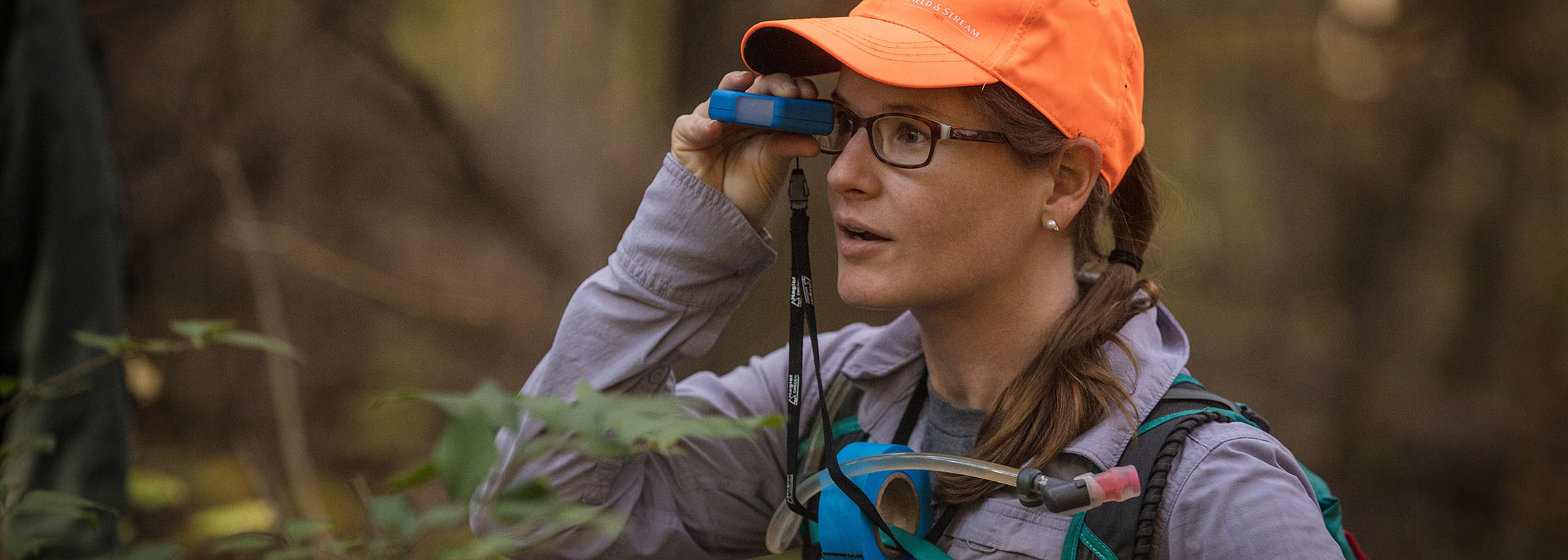 IMBA trail planner with purple jacket and orange hat holds clinometer to eye to assess slope angle