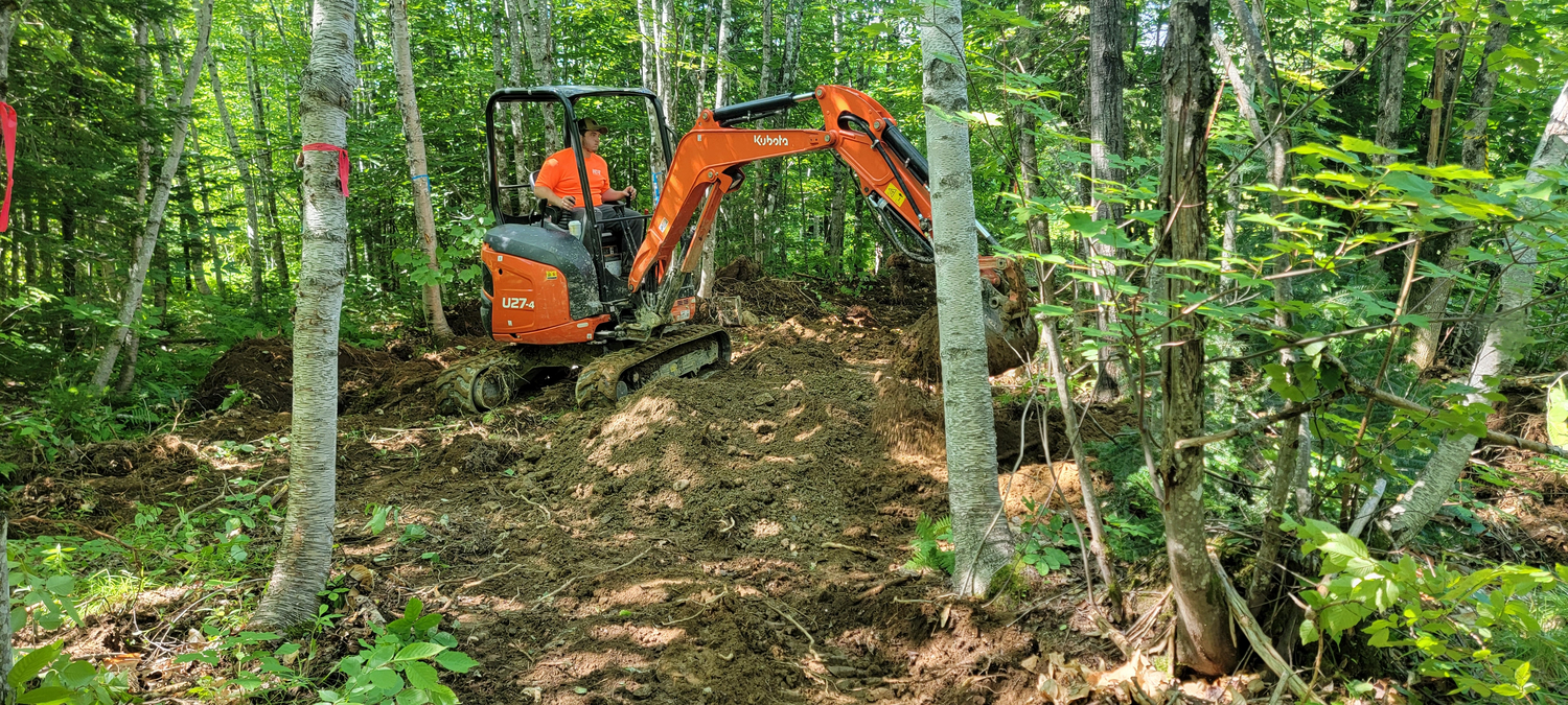 "A person in an orange excavator builds trails"