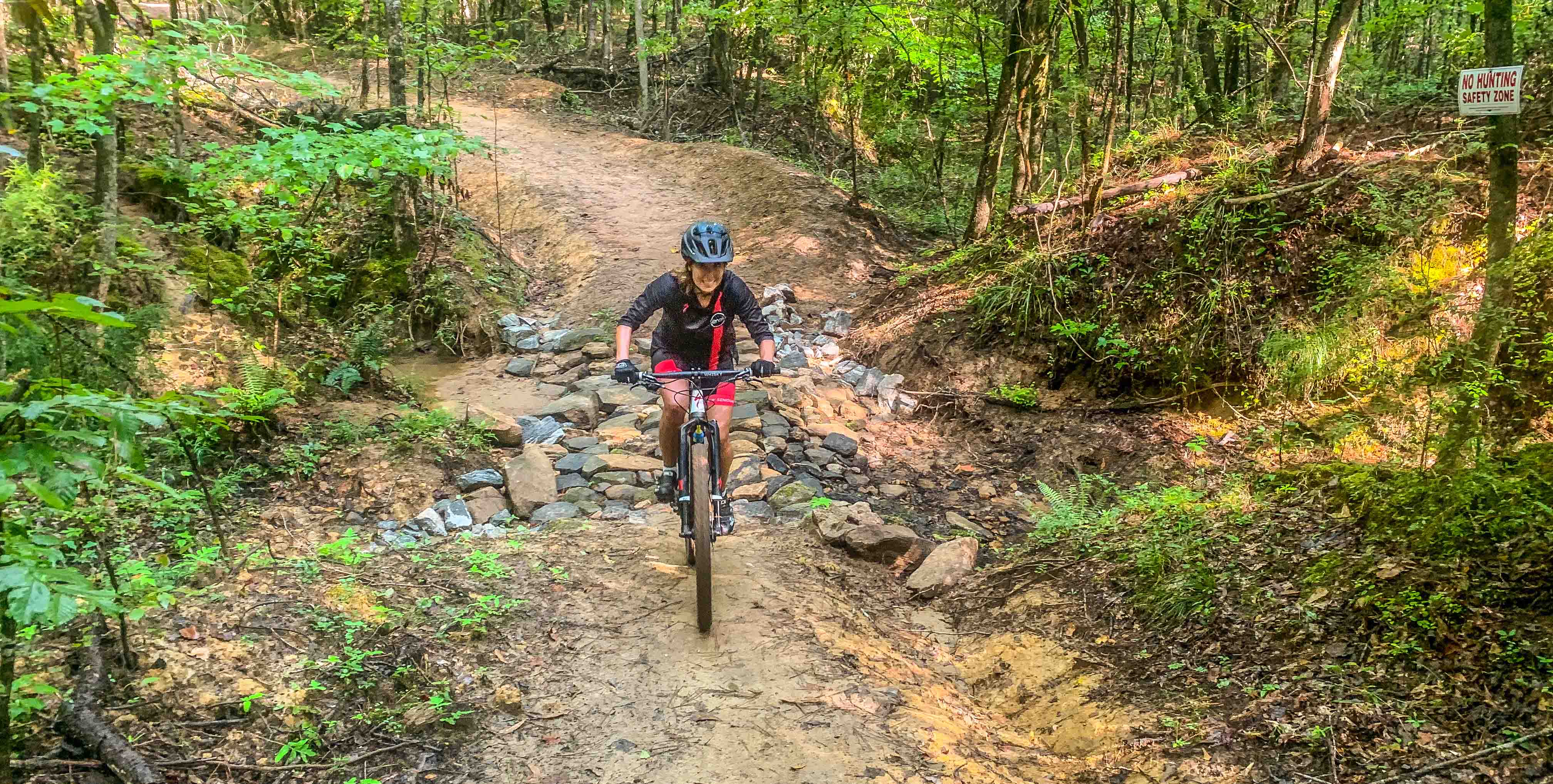 Rider on trail clearing short rocky section amidst spring foliage 