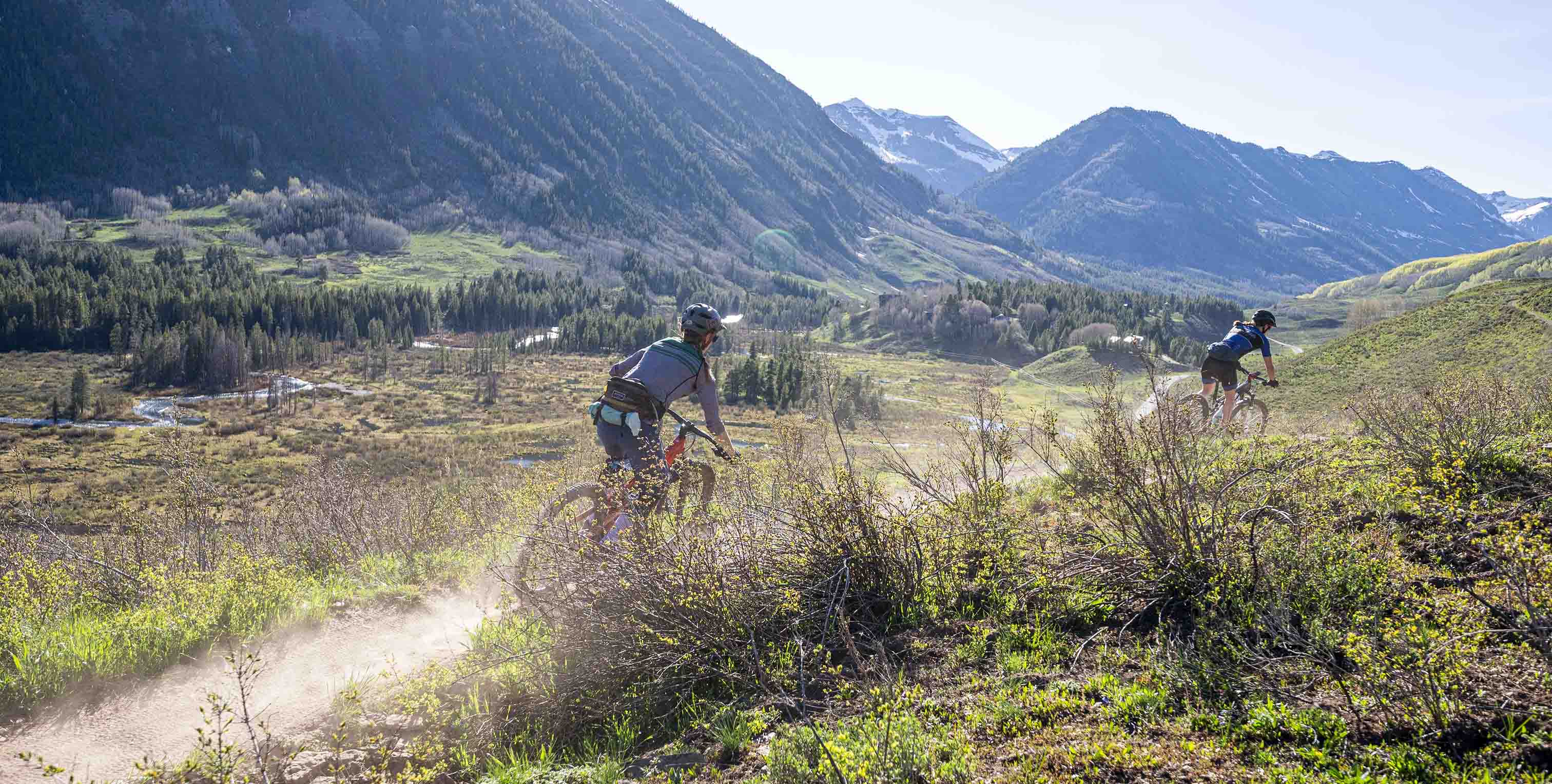 Two female riders riding away from frame with valley and homes in foreground, green mountains in background