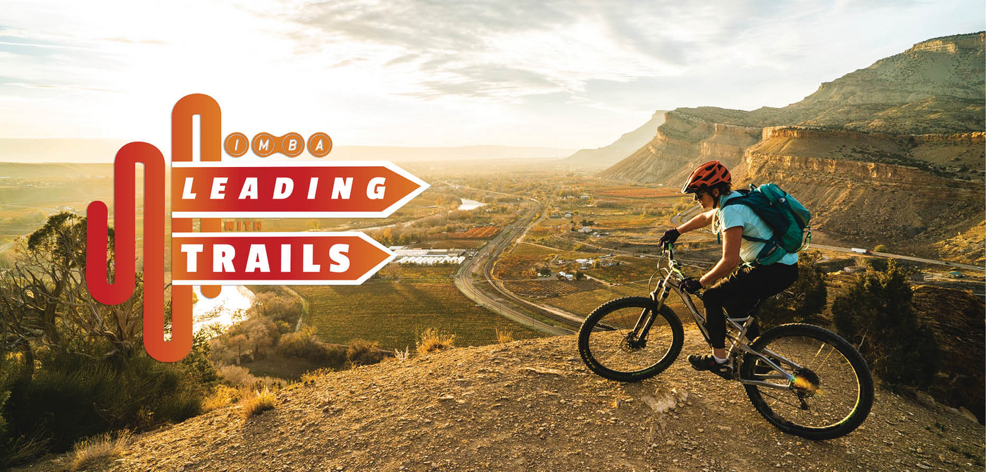 Leading with trails, mountain biker overlooks trail friendly community on trail. 
