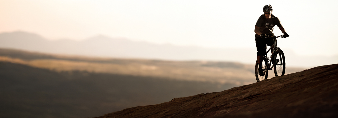 mountain biker riding on a rocky ridge with mountains in the background