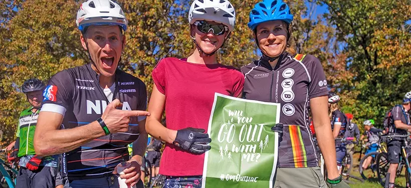 Engage with local partners and affiliates, three people posing with a flyer in mountain biking gear. 