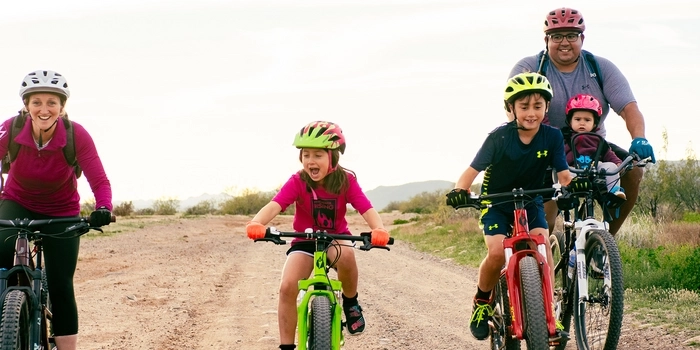 Family ride consisting of an adult female, and adult male riding with a baby, and two young mountain bikers on a gravel road. 