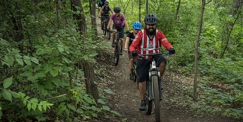 Five riders of various ages riding mountain bikes on a lush green trail in Omaha, Nebraska