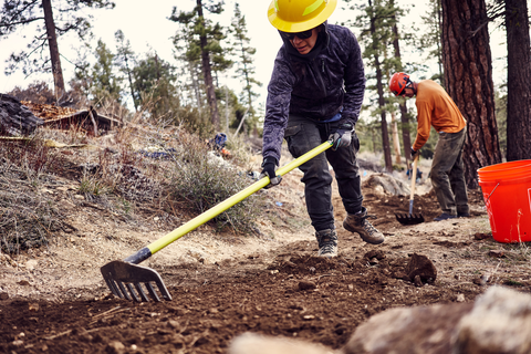 Two trail builders wearing helmets, digging in fresh dirt on a single track mountain bike trail in Lowe Lifes area during the USFS Summit.