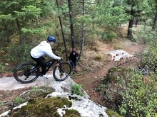 Lady mountain biker contemplating a medium rock drop while another rider monitors.
