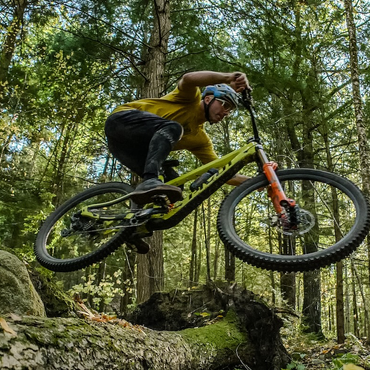 Brice Shirbach, IMBA's Communication Manager riding a mountain bike on trail jumping over a log in Claremont, New Hampshire. 