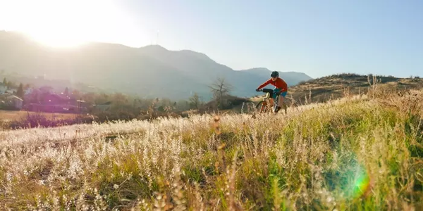 rider wearing red pedaling along a ridge with the sun in the background 