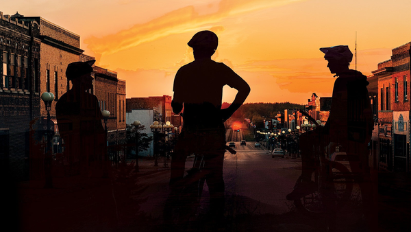 Three mountain bikers ending a ride at sunset with the backdrop of a main street downtown